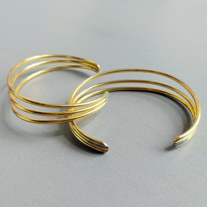 May include: Three gold-toned metal bangles stacked on top of each other. The bangles are simple and have a smooth, polished finish.