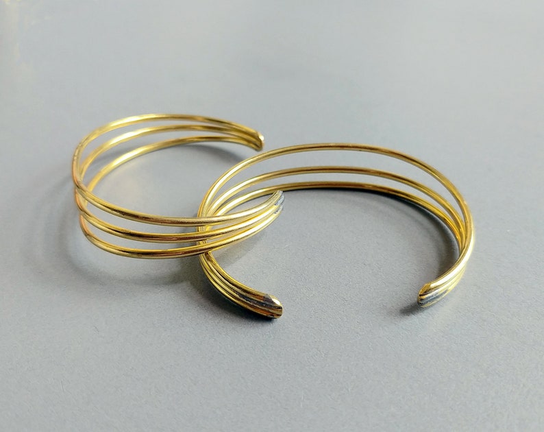 May include: Three gold-toned metal bangles stacked on top of each other. The bangles are simple and have a smooth, polished finish.