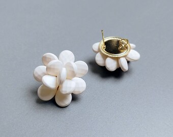 May include: A pair of white flower-shaped earrings with gold-toned backs. The earrings are made of small, round, white beads that are clustered together to form a flower shape.