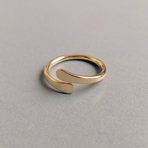 May include: A gold-toned ring with a unique design, featuring a curved band that wraps around the finger and a smaller band that overlaps it.