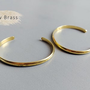 Puede incluir: Dos brazaletes simples de metal de color dorado. El texto "Raw Brass" es visible en la imagen.