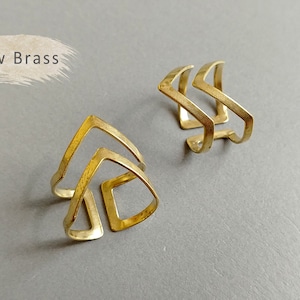 May include: Two gold-toned metal rings with a geometric arrow design. The rings are made of raw brass.