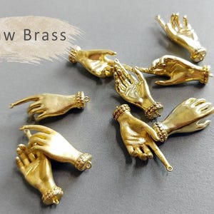 May include: Raw brass hand charms with a textured finish. The charms are in the shape of a hand with the fingers pointing in different directions.