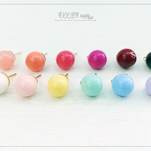 May include: Assortment of 12 round, colourful, glass earring studs. The studs are in various colours, including white, pink, light blue, yellow, red, and black.