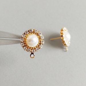 Puede incluir: Un par de pendientes de tono dorado con una perla y detalles de diamantes de imitación transparentes.