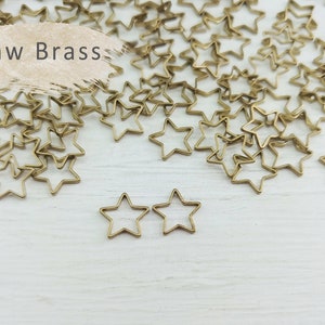 Könnte beinhalten: Rohe Messing-Stern-Anhänger, verstreut auf einer weißen Oberfläche. Der Text "Raw Brass" ist in der oberen linken Ecke des Bildes sichtbar.
