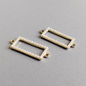 May include: Two gold-toned rectangular frames with a pearl border. The frames have a small loop at each corner.