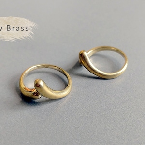 May include: Two gold-toned rings with a unique curved design. The rings are made of raw brass and have a simple, minimalist aesthetic.