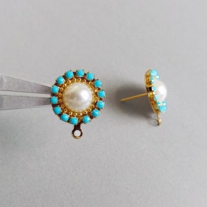 May include: A pair of gold-colored stud earrings. Each earring features a central white pearl surrounded by small turquoise-colored stones. The earrings have a post and loop design for attachment.