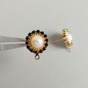 Puede incluir: Un par de pendientes de botón dorados. Cada pendiente presenta una perla blanca central rodeada por un anillo de pequeñas piedras preciosas de color azul oscuro. Los pendientes tienen un diseño de poste y bucle.