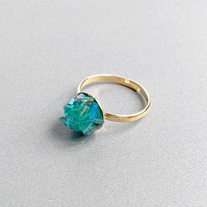 May include: A gold ring with a teal blue crystal gemstone. The crystal is faceted and has a geometric shape.
