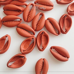 May include: A collection of terracotta-colored clam shell beads. The beads are oval-shaped with a textured surface and a detailed, open design. These beads are suitable for jewelry making and craft projects.