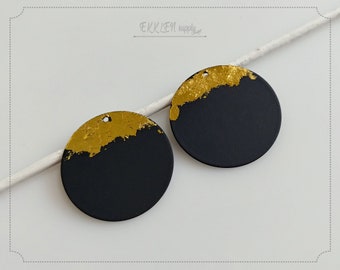 May include: Two round black and gold painted wood or polymer clay embellishments with a hole for hanging. The gold paint is applied in a textured, uneven, and abstract pattern.