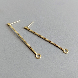 Può includere: Un paio di orecchini dorati con un design a filo ritorto e un piccolo anello all'estremità di ogni filo.