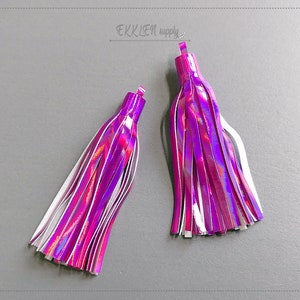 May include: Two iridescent purple and white tassels with a shiny finish. The tassels are approximately 5 cm long.