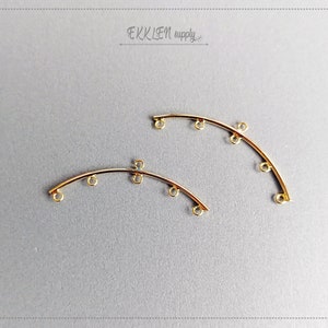 Puede incluir: Dos piezas conectoras curvas de metal dorado con cinco anillos de salto cada una. Las piezas conectoras son ideales para la elaboración de joyas.