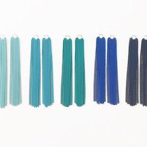 May include: Six pairs of long, dangling earrings with chain links. The earrings are in shades of blue, teal, and green.