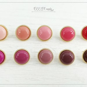 May include: Ten round, flat, gold-rimmed buttons in various shades of pink, red, and brown. The buttons are arranged in two rows of five.