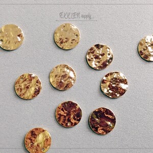 May include: Ten gold-colored metal round discs with a hammered texture. Each disc has two small holes near the top.