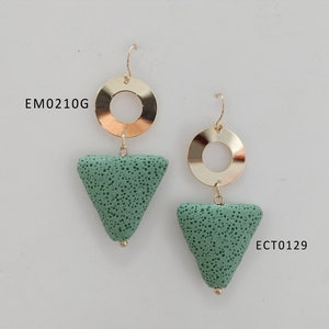 May include: A pair of gold-colored earrings with a circular top and a triangular, porous, seafoam green stone pendant. The earrings have a hook closure. The text "EM0210G" and "ECT0129" are visible.