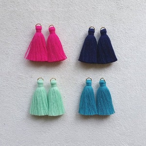 May include: Four pairs of colourful tassels with gold rings. The tassels are pink, blue, light blue, and turquoise.