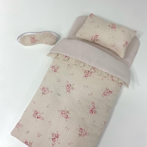Könnte beinhalten: Ein rosa-weißes Puppenbett mit floralem Muster, einem passenden Kissen und einer rosa Augenmaske.