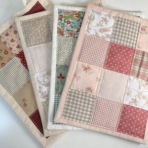 Peut inclure: Quatre maniques matelassées avec un motif patchwork. Chaque manique présente différents motifs de tissu, notamment des motifs floraux, rayés et à carreaux. Les maniques sont dans les tons de rouge, beige et rose, avec une bordure crème.