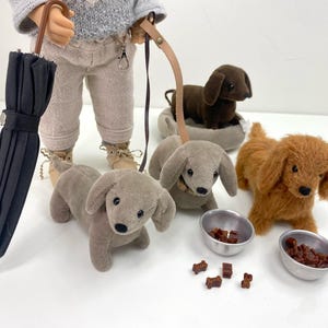 May include: A doll wearing a grey sweater and holding a black umbrella walks three toy dogs on leashes. Two of the dogs are grey and one is brown. The dogs are sitting in front of their food bowls.