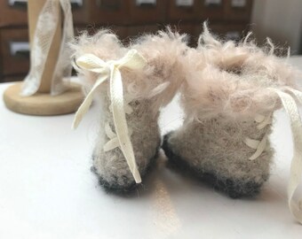 May include: A pair of fuzzy, light brown baby booties with white laces and a white bow on the top of each boot.