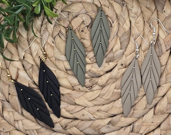May include: Three pairs of dangle earrings with leaf-shaped charms. The earrings are made of black, green, and brown clay and have gold accents.
