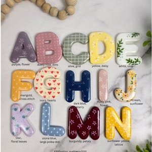 May include: A collection of fourteen individual alphabet letters A through N, each featuring unique colours and patterns including floral, polka dot, grid, heart, and lattice designs. Each letter is labelled with its specific colour and pattern name.