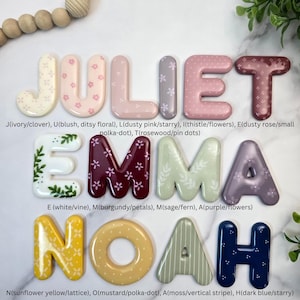May include: A collection of three-dimensional letters spelling JULIET, EMMA, and NOAH. Each letter features a unique colour and pattern, including floral, polka-dot, vine, lattice, and striped designs in shades of ivory, pink, purple, green, yellow, and blue.