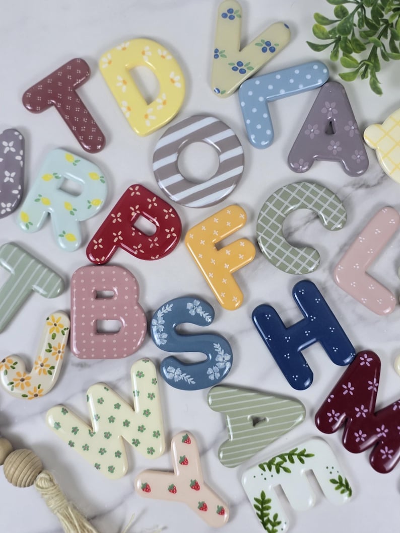 May include: A collection of colourful alphabet letters featuring various patterns including floral, polka dot, striped, and checkered designs. The letters are rendered in shades of yellow, blue, pink, red, green, and brown with a smooth finish.