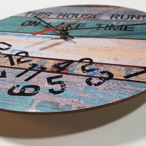 Puede incluir: Un reloj redondo de madera con un acabado pintado desgastado. La esfera del reloj tiene n&uacute;meros negros y el texto "This house runs on lake time".