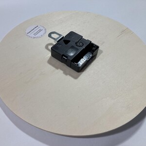 Puede incluir: La parte posterior de un reloj redondo blanco con un mecanismo de reloj negro adjunto. El mecanismo del reloj tiene una peque&ntilde;a pegatina que dice "Crazy Clock Shop".