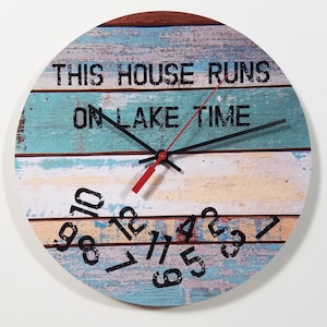 May include: A round wooden clock with a blue, white, and brown striped design. The clock face has black numbers and hands, and the text "This house runs on lake time".