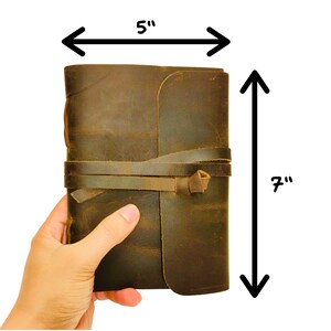 May include: A brown leather journal with a strap closure. The journal measures 5 inches wide and 7 inches tall.