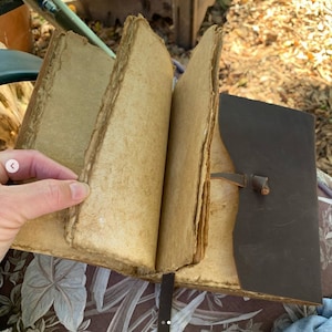 Puede incluir: Un diario encuadernado en cuero marr&oacute;n con p&aacute;ginas en blanco. El diario est&aacute; abierto y las p&aacute;ginas est&aacute;n ligeramente amarillentas. El diario tiene una correa de cuero con una hebilla.