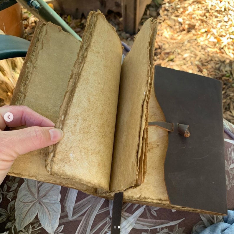 Puede incluir: Un diario encuadernado en cuero marr&oacute;n con p&aacute;ginas en blanco. El diario est&aacute; abierto y las p&aacute;ginas est&aacute;n ligeramente amarillentas. El diario tiene una correa de cuero con una hebilla.