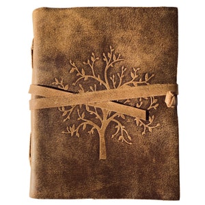 May include: A brown leather journal with a tree design embossed on the front cover. The journal is closed and has a brown leather strap with a knot on the right side.