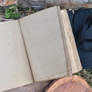 May include: An open, blank, cream-coloured journal with worn edges. The journal is lying on a wooden surface.