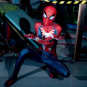 May include: A red and blue Spider-Man costume with a white spider emblem on the chest. The costume features a red mask with white eye lenses and a webbed design. The person is in a crouching position.