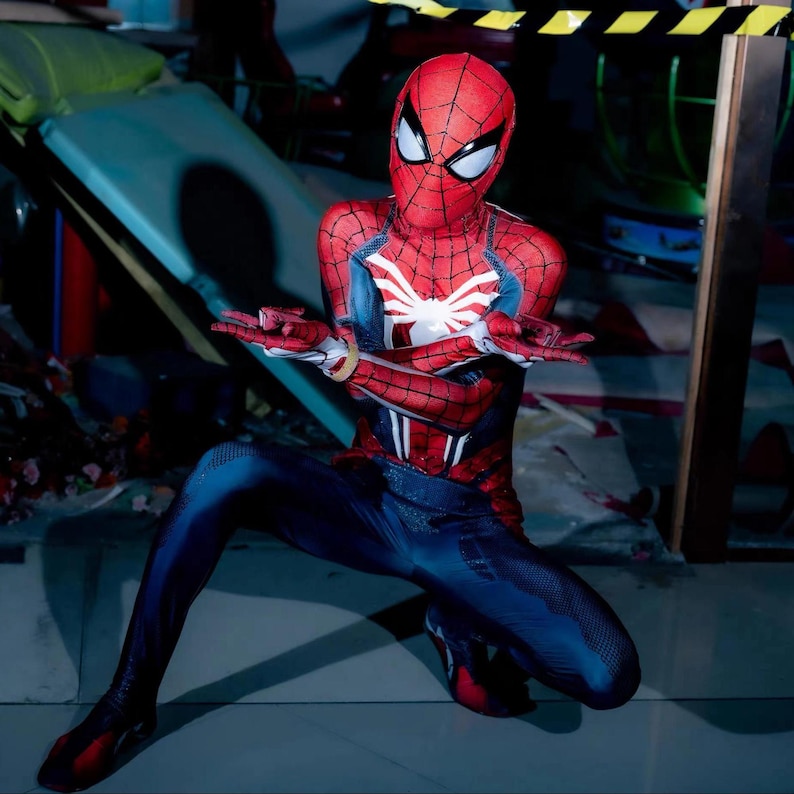 May include: A red and blue Spider-Man costume with a white spider emblem on the chest. The costume features a red mask with white eye lenses and a webbed design. The person is in a crouching position.