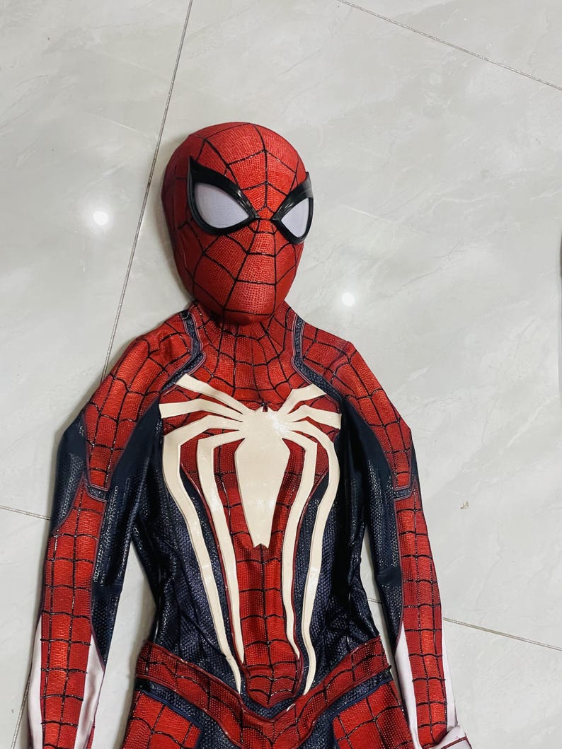 May include: A red and black Spider-Man costume with a white spider emblem on the chest. The costume features a web pattern and a mask with white eye lenses. The suit is designed to resemble the superhero's iconic look.