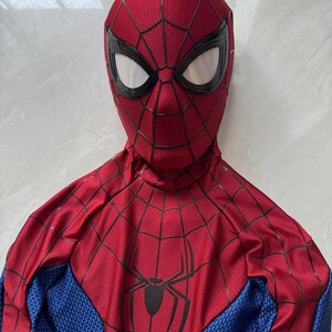 Puede incluir: Un disfraz de cuerpo completo que presenta una m&aacute;scara roja con patrones de telara&ntilde;a negros y grandes lentes oculares de malla blanca. El torso es rojo con un emblema de ara&ntilde;a negro y detalles de telara&ntilde;a, con mangas y laterales azules.