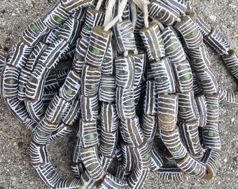 May include: A strand of brown and white ceramic beads with green accents. The beads are cylindrical and have a striped pattern.