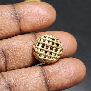 May include: A gold-colored metal bead with a lattice design. The bead is round and has a slightly raised surface.