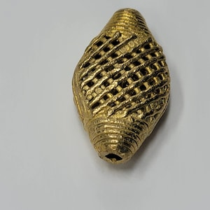 May include: A gold-colored metal bead with a woven, lattice-like design. The bead is shaped like a teardrop or a cone.