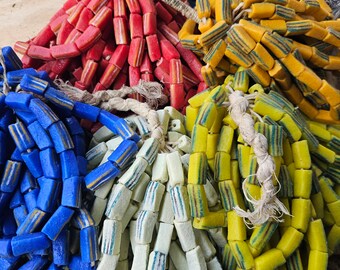 May include: Assortment of colorful glass beads, including blue, red, yellow, and green. The beads are arranged in a pile and are made of various sizes and shapes.