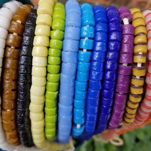 May include: A collection of colorful glass beads, each strand featuring a different pattern and color. The beads are round and have a slightly textured surface. The colors include teal, white, brown, black, yellow, green, light blue, dark blue, purple, yellow and orange.